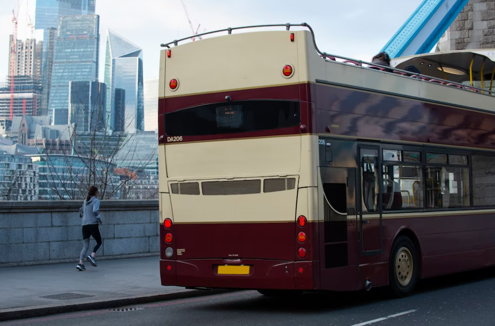 red and beige double-decker bus on the road, sunning woman and skyscrapers behind