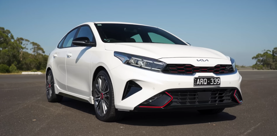 white car kia cerato on the road and trees behind