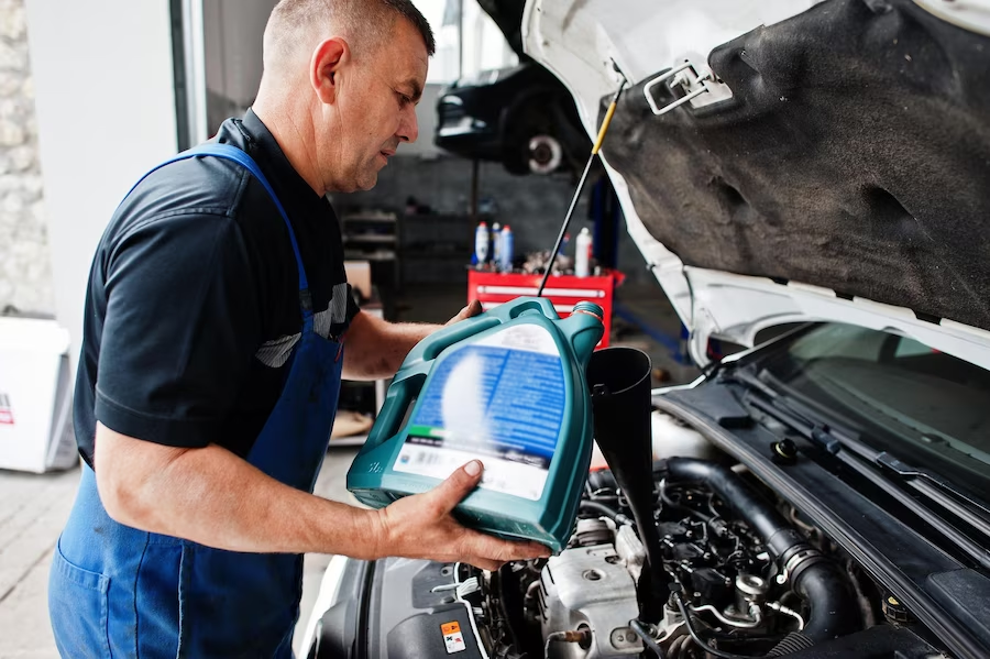 Mechanic in uniform pouring new oil at auto service