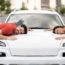 A man and a woman resting their heads on a car hood, smiling