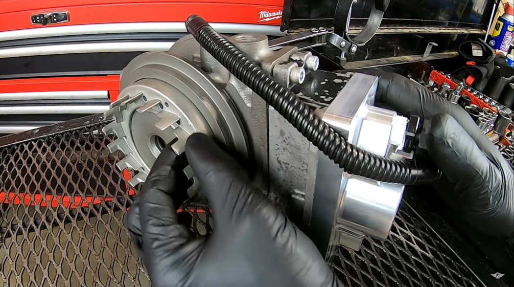 hand in black gloves holding car component, red car behind