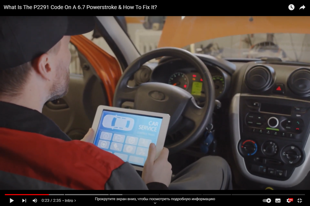 A male mechanic sits inside the car and fixes an engine error, holding a tablet