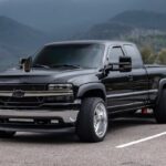 A black car on high wheels stands against mountains